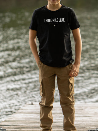 Person wearing a black t-shirt with 'Three Mile Lake' text standing on a dock by water.